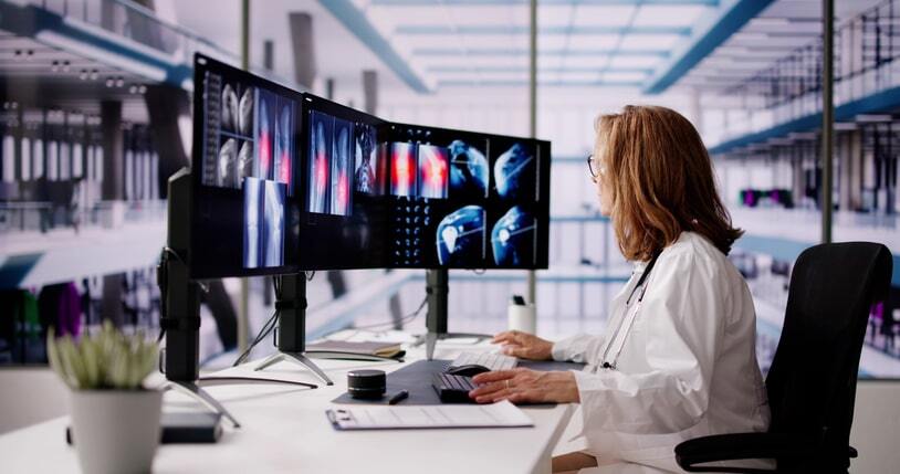 A radiologist uses multiple computer monitors to analyze medical images using an advanced PACS imaging system, integrated with RIS software to streamline radiology workflows and enhance patient care.