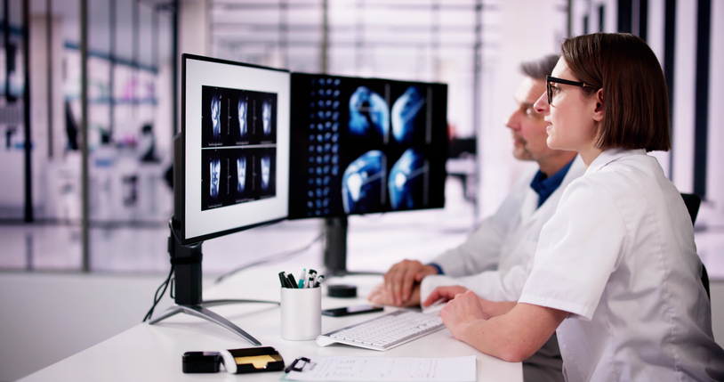 Two doctors reviewing medical imaging results on multiple computer monitors, using a advanced PACS software for diagnostic purposes.